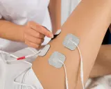 Elektrostymulacja efekty uda: terapeuta umieszcza elektrody na udzie pacjentki, przygotowując do zabiegu.