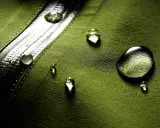 Gocce d'acqua su tessuto verde, dimostrando il significato di "water repellent".