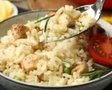 Kremowe risotto z kurczakiem, groszkiem i rozmarynem, udekorowane pomidorkiem. Idealne na obiad.