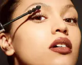 Una mano aplica máscara de pestañas a unos ojos pequeños, resaltando su belleza natural.