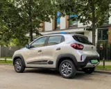 Srebrny Dacia Spring, elektryczny samochód miejski, parkuje pod drzewami. Jego zasięg pozwala na swobodne poruszanie się po mieście.
