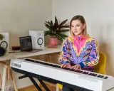 Kobieta gra na pianinie Yamaha. W tle laptop i głośniki, idealne do nauki śpiewu dla dzieci.
