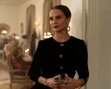 Alicia Vikander i en elegant svart klänning med stora örhängen, håller ett glas. Scenen utspelar sig på en tillställning, kanske från en av hennes filmer.