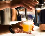 Ręka nalewa złociste piwo do szklanki. Czy alkoholik może pić piwo bezalkoholowe? To pytanie, na które odpowiedź zależy od indywidualnej sytuacji.