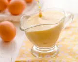 Crema pastelera cremosa en una salsera de cristal, con huevos frescos al fondo.