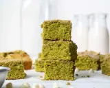 Grüne, saftige matcha brownies, gestapelt und auf einem Tisch arrangiert, mit weißen Schokostückchen und Milchflaschen im Hintergrund.