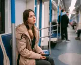 Młoda kobieta w beżowej kurtce siedzi w metrze, zamyślona. Może właśnie wraca z wizyty u lekarza, który wystawił jej L4 z powodu wypalenia zawodowego.