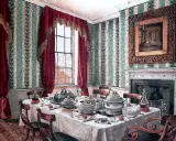Salle à manger élégante avec table dressée pour un service à la française, droite ou gauche. Papier peint rayé vert et blanc, rideaux bordeaux.
