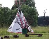 Wioska indiańska na Mazurach z tipi ozdobionym zwierzętami, bocianem i łukami.
