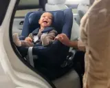 Bebé sonriente en un maxicosi azul, listo para aprender como colocar el maxicosi en el coche.