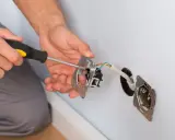 Instalacja gniazdka z uziemieniem. Ręce przykręcają mechanizm do puszki, podłączając przewody.