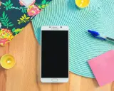 Un smartphone prêt à vous aider à vous organiser au quotidien. Un carnet fleuri, des bougies, un stylo et un post-it rose complètent la scène.