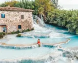 Cascate naturali con acqua turchese, una donna seduta su una roccia. Un antico mulino in pietra sullo sfondo. Tra le terme più belle d'Italia.
