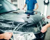 Profesjonaliści nakładają folię ochronną na maskę czarnego auta. To kluczowy etap car wrappingu, chroniący lakier.