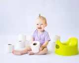 Uśmiechnięte dziecko bawi się papierem toaletowym obok zielonego nocnika. Czas na naukę korzystania z nocnika!