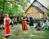 En grupp människor i vikingakläder samlas framför ett trädhus i vikingabyn Storholmen.