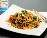 En tallrik med nudlar och grönsaker, perfekt för ett snabbt wok recept. Hoisinsåsburk syns i bakgrunden.