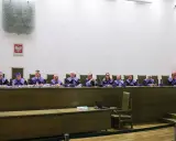 Sędziowie w togach siedzą za stołem w sali sądowej, przygotowując się do rozprawy przed trybunałem stanu.