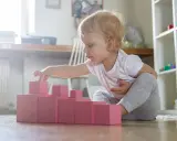 Bambina bionda gioca con blocchi rosa, ideali come giochi montessori 6 mesi fai da te per sviluppare la coordinazione.