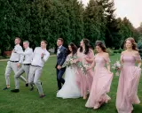 Para ślubna z drużbami i druhnami w eleganckim ubiorze na ślub, idący przez trawnik.
