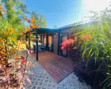 Uroczy tiny house wynajem. Drewniany domek z tarasem, otoczony zielenią i kwitnącymi krzewami. Idealne miejsce na relaks.