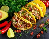 Pyszne dania meksykańskie: tacos z mielonym mięsem, serem, pomidorami i awokado, ozdobione papryczkami chili i limonką.