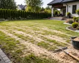 Piaskowanie trawnika w trakcie prac pielęgnacyjnych. Grabie i wiadro z piaskiem czekają na dalsze działania.