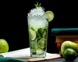 Orzeźwiający mojito przepis: szklanka pełna lodu, mięty i limonki, obok jabłka i książki. Idealny na letnie popołudnie.