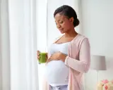 Femme enceinte tenant un verre de jus vert, caressant son ventre. Elle prend soin de sa peau sèche pendant la grossesse.