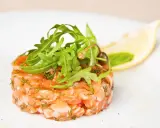 Un délicieux tartare de saumon frais, garni de roquette et d'une tranche de citron, prêt à être dégusté.