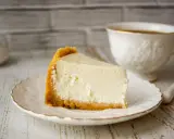 Kawałek kremowego sernika na kruchym spodzie, przygotowanego z mlekiem z puszki, czeka na talerzyku obok filiżanki kawy.