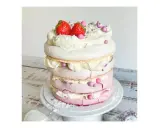 Eine mehrstöckige Baiser Torte mit Sahne, Erdbeeren und rosa Zuckerperlen.