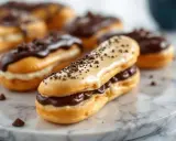 Éclairs gourmands, parfaits après le temps de cuisson pâte à choux. Garnis de crème et nappés de chocolat, ils sont prêts à être dégustés.
