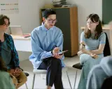 Grupa młodzieży na sesji terapeutycznej. Psycholog notuje, a dziewczyna z protezą ręki uważnie słucha. Rozmowa o tym, co po psychologii.