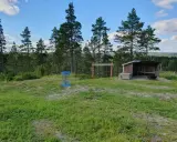 En blå discgolfkorg står på en gräsklädd kulle med skog i bakgrunden. En vindskyddad rastplats finns i närheten. Perfekt för discgolf i Hudiksvall.