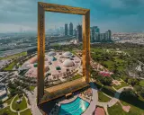 Dubai Frame rahmt die Skyline und die futuristischen Dubai Projekte ein. Ein Park mit Kuppeln und ein Pool sind im Vordergrund.