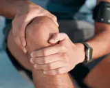Mężczyzna trzyma się za kolano, zastanawiając się, jak długo trwa rehabilitacja po endoprotezie kolana.