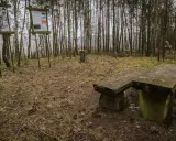 Kamienny stół i ławka w lesie, obok tablice informacyjne. Miejsce na odpoczynek podczas wędrówki po górach obkaskich.