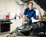 Mecánica muestra cómo cambiar el aceite del coche, sosteniendo una botella de aceite Repsol Master.