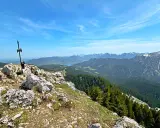 Gipfelkreuz am Fockenstein bei Lenggries, mit Blick über Wälder und Berge bis zum See.