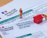 Figurines sur des documents fiscaux français. L'une pousse une maison rouge, symbolisant la taxe foncière pour un revenu modeste.