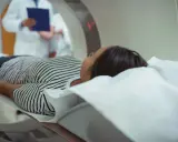 Pacjentka leży na łóżku rezonansu magnetycznego, obok niej stoi lekarz z dokumentacją.