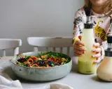 En skål med färgglad sallad och två flaskor dressing till sallad. En flicka håller i den ena flaskan.