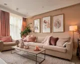 Un salon coloré et chaleureux, avec un canapé beige, des coussins roses et des tableaux de feuilles.