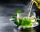 Un thé fumant à la menthe poivrée est versé dans une tasse transparente, ornée d'une feuille de menthe fraîche.
