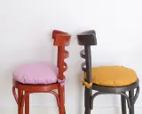Dos sillas de madera pintadas, una roja con cojín lila y otra gris con cojín ocre. ¡Ideas para pintar sillas de madera!