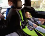 Uśmiechnięte dziecko w foteliku samochodowym zgodnym z normą i-Size, podróżujące bezpiecznie z mamą.