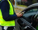 Osoba w kamizelce odblaskowej używa alkomatu. Wiesz, jak anonimowo zgłosić pijanego kierowcę?