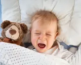 Bebé llorando en la cama con su osito de peluche. Mi hijo de 2 años se despierta mucho por la noche.