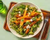 Pâtes vertes avec des carottes rôties et du fromage émietté, garnies de fanes de carottes fraîches.
